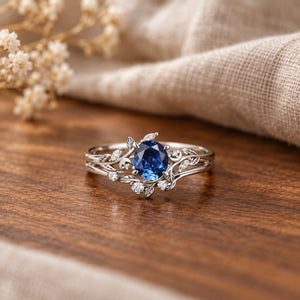 Lab sapphire leaf-and-moon engagement ring set on warm walnut tabletop