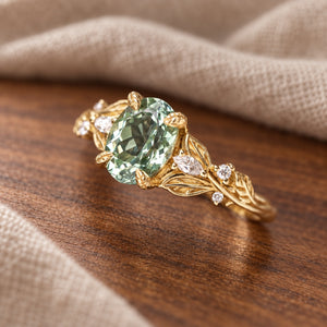 Kimberly oval-cut green sapphire leaf-and-vine milgrain engagement ring on warm walnut tabletop