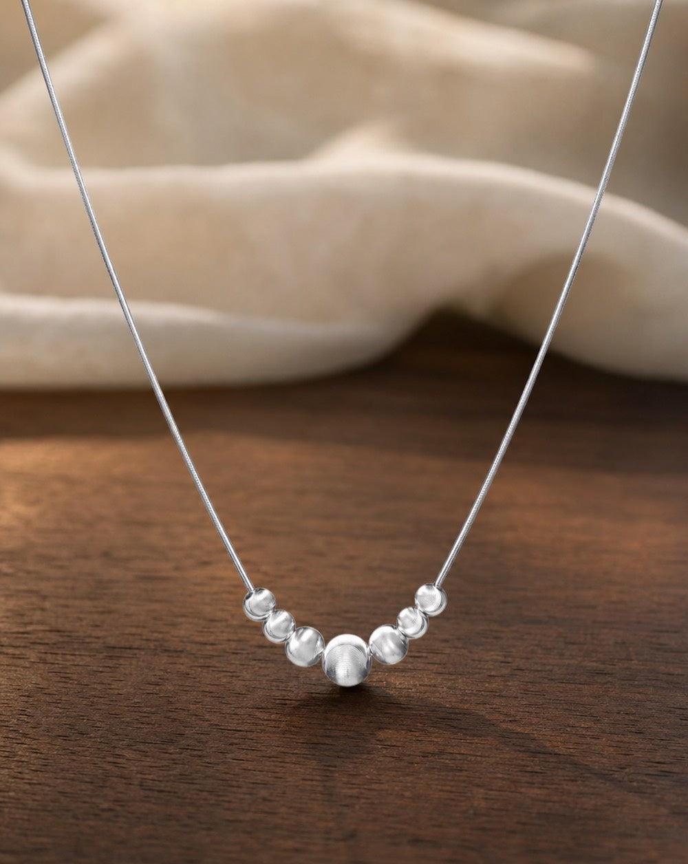 Silver Chatoyancy Ball Bead Charm Necklace on warm walnut surface