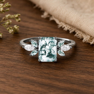 Black Gold Emerald Cut Moss Agate Butterfly Fairy Engagement Ring on walnut tabletop