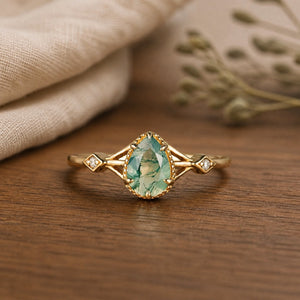 Pear dainty moss agate engagement ring on a warm walnut tabletop