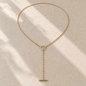 Gold beaded lariat toggle necklace with moissanite ring and bar pendant on pale stone