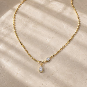 Gold bead-chain necklace with pear-shaped moissanite pendants on pale stone