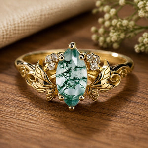 Daphne's Laurel Marquise Moss Agate with Moissanite Leaves Engagement Ring on walnut tabletop