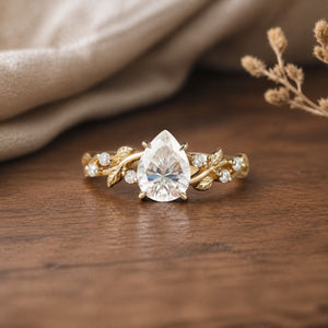 Moissanite leaf engagement ring by Hebe on a warm walnut tabletop