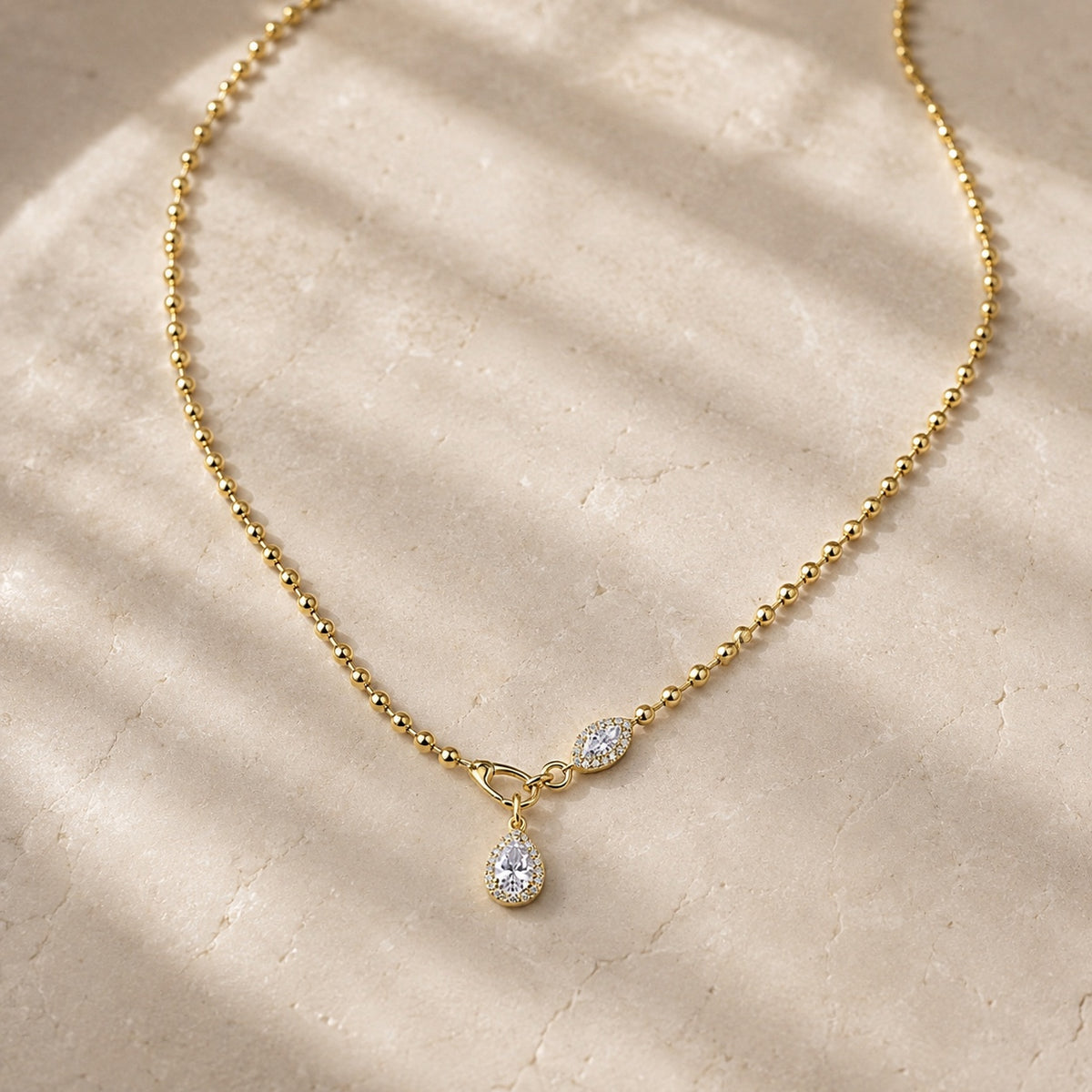 Gold bead-chain necklace with pear-shaped moissanite pendants on pale stone