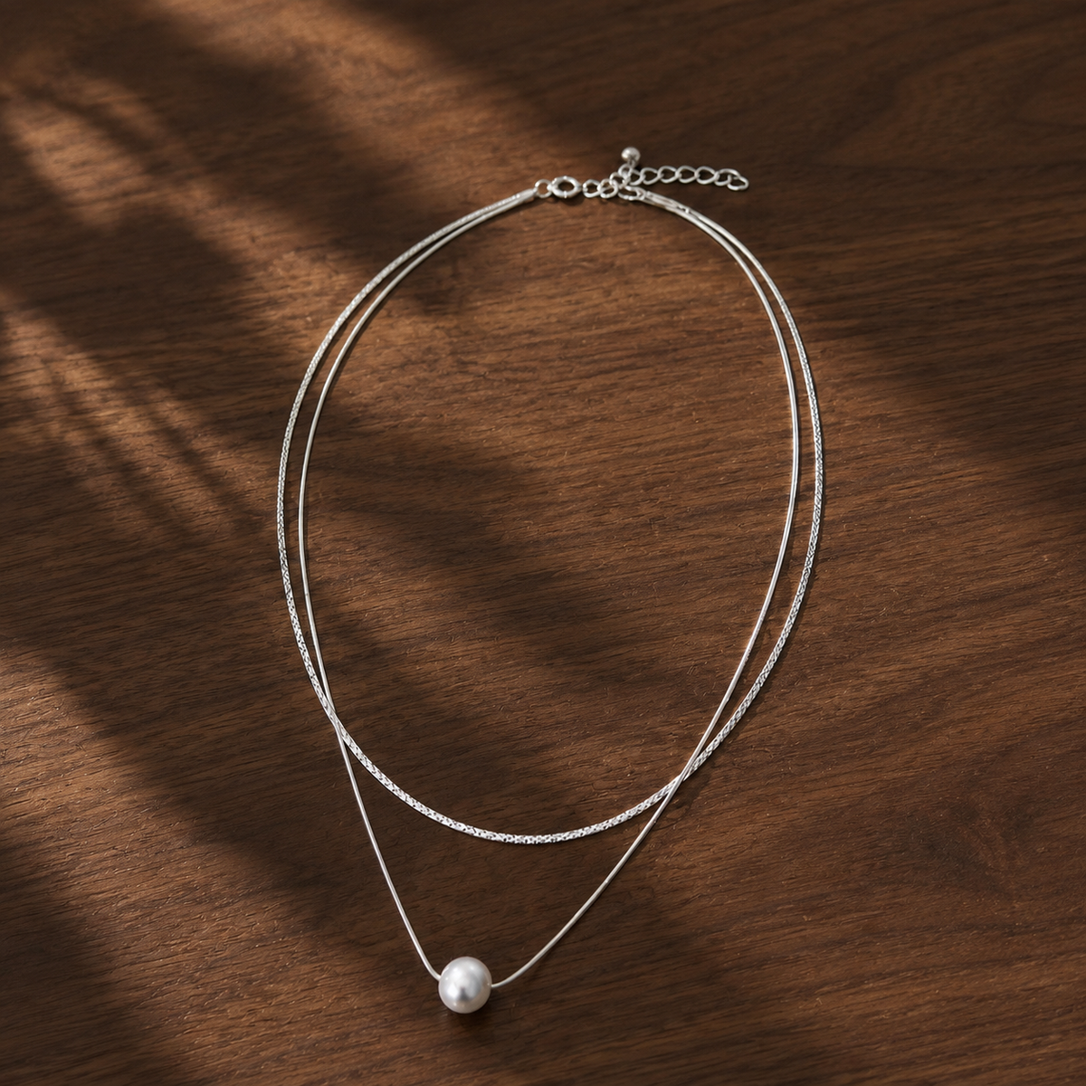 Layered silver ball-bead necklace with pearl pendant on walnut tabletop