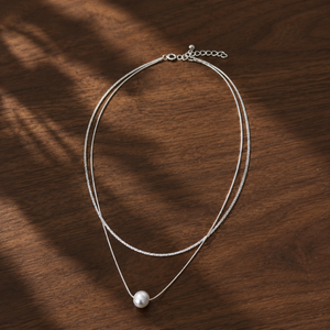 Layered silver ball-bead necklace with pearl pendant on walnut tabletop
