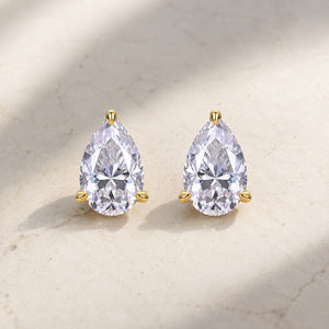 Pair of pear-shaped clear moissanite stud earrings with gold prongs on pale stone