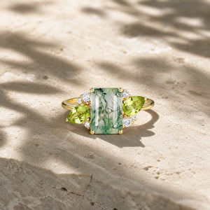 Emerald-cut moss agate engagement ring with pear-shaped peridot and moissanite accents on warm stone
